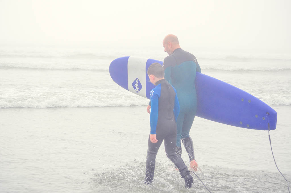 Boy walking into water with surfboard and instructor