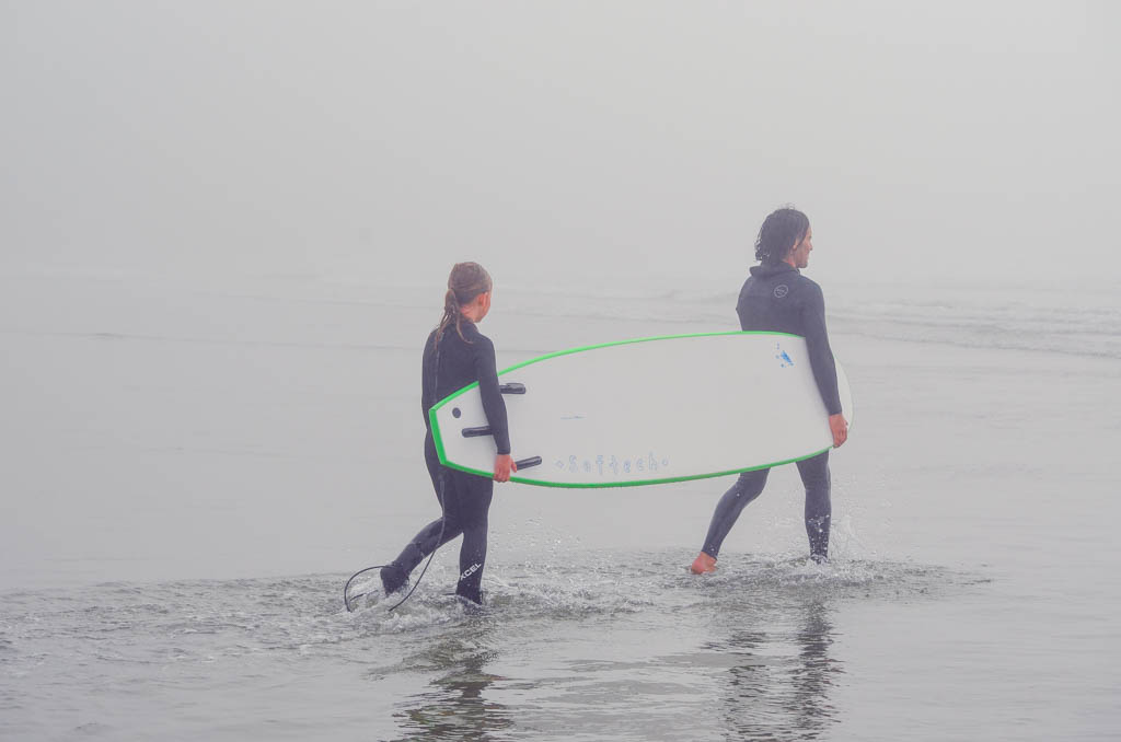 Girl walking into water with instructor and surfboard 