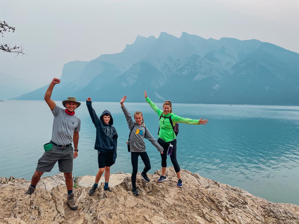 hiking guide and family standing on top of a large rock in front of a lake
