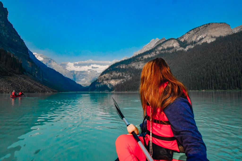woman turned looking at the scenery behind her while sitting in a canoe on lake louise