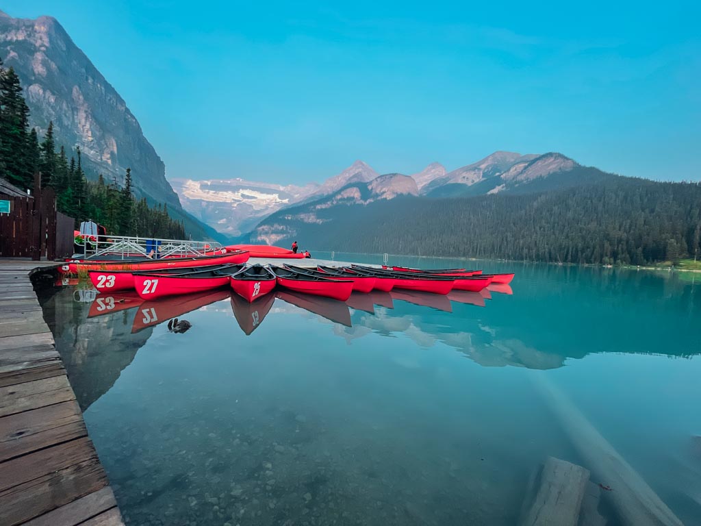 group of red canoes floating on a blue coloured lake louise with the mountains in the background