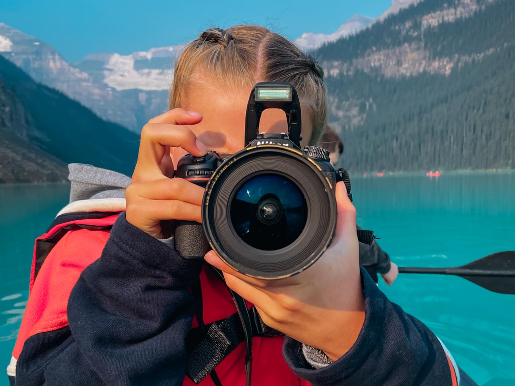 girl pointing her camera lens at the photographer with lake louise in the background