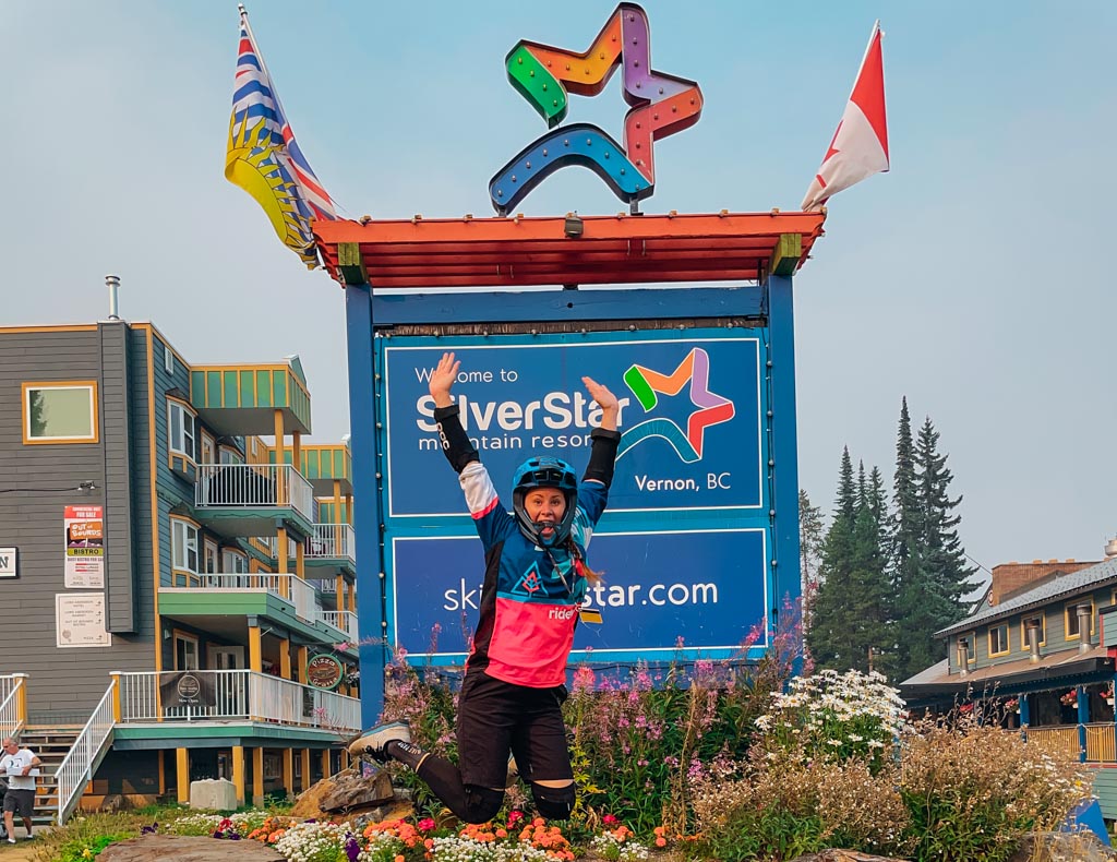woman wearing mountain biking gear jumping in front of silverstar mountain sign